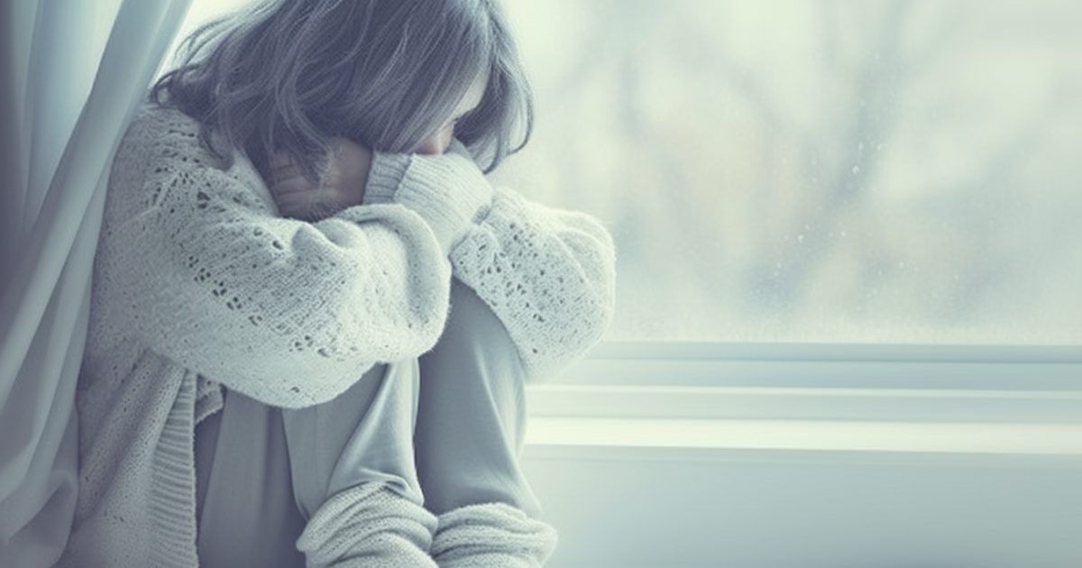 窓辺に座り、膝を抱えてうつむく女性。寒色系の淡い光が静寂を演出し、寂しさと内省的な雰囲気を醸し出すリアルなAIイラスト。